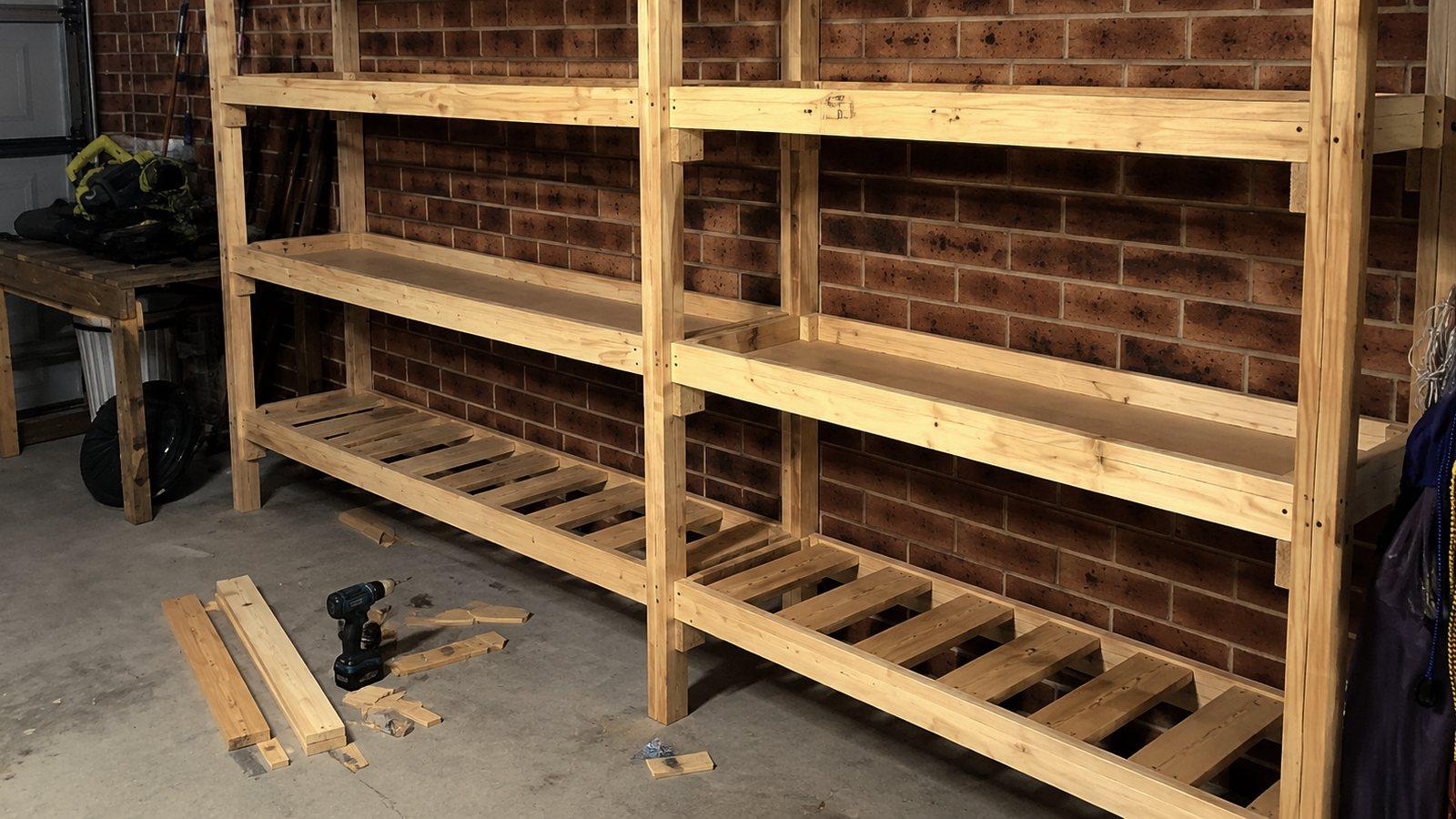 A timber storage shelving wall part way through a build in a garage, drill and offcuts on the floor