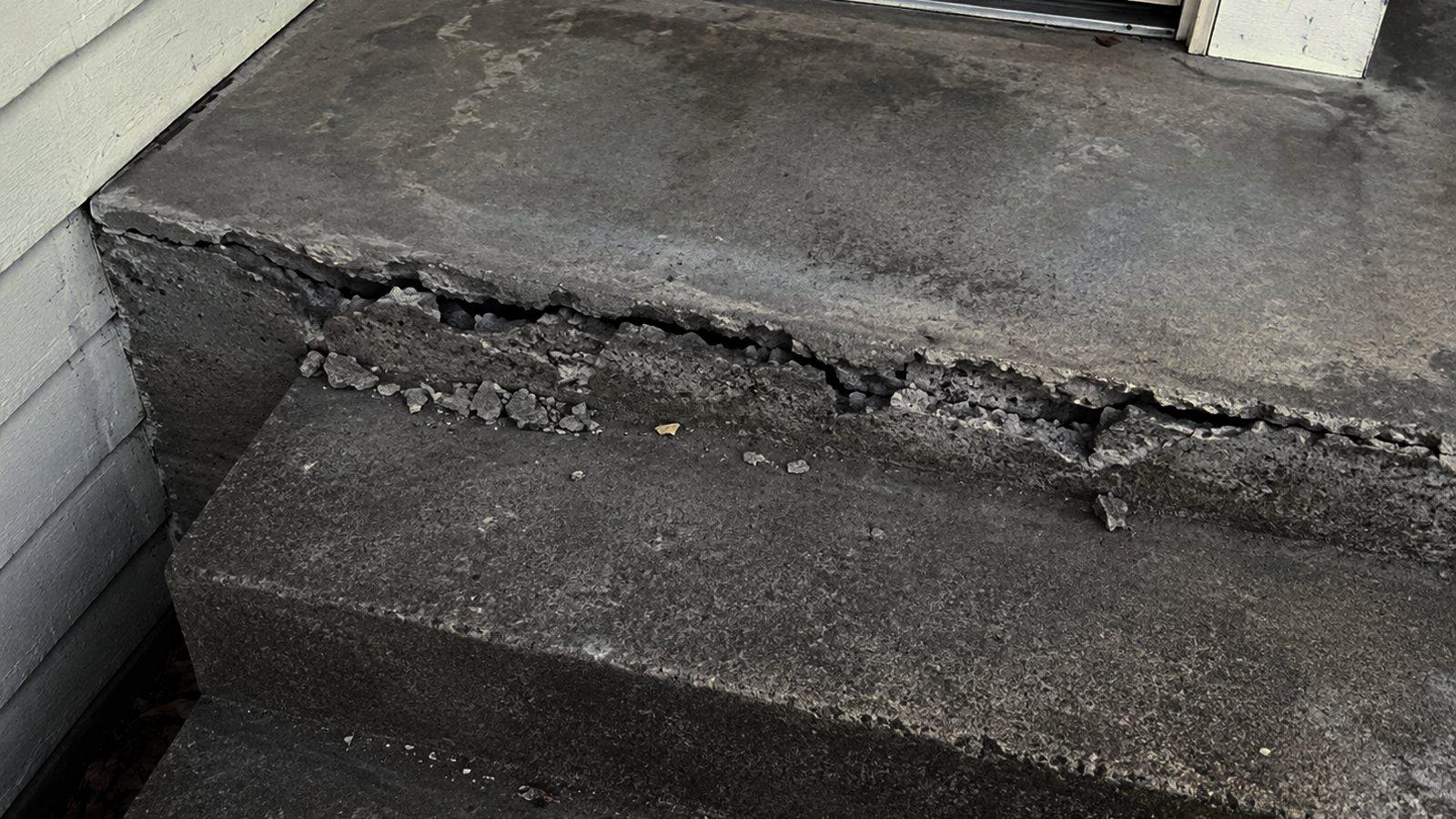 A concrete doorstep at a brick unit with its edge broken away and rubble on the ground