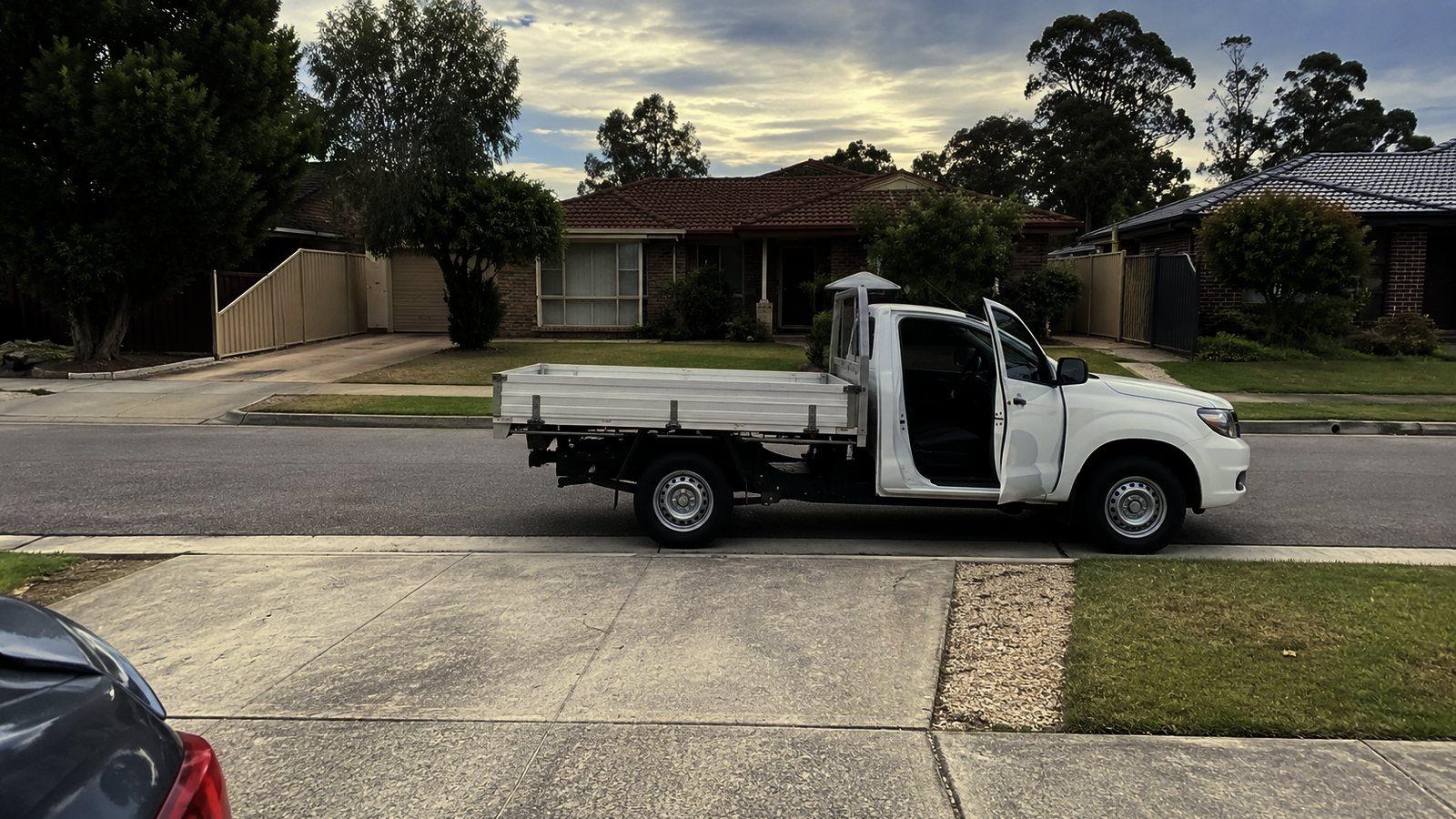 A work ute parked at the kerb outside a suburban house with the driver door open