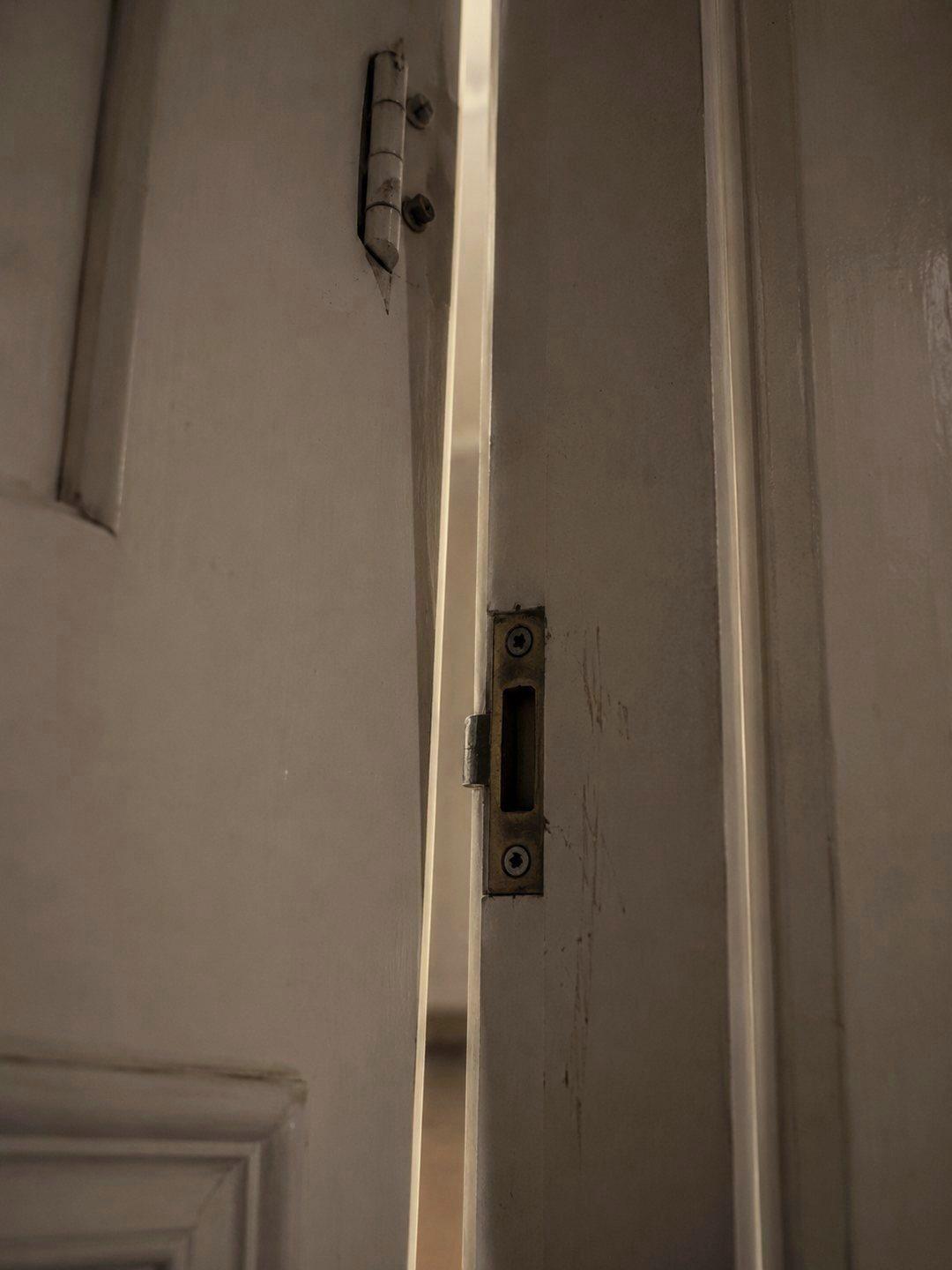 An internal door stopped short of closing, the gap uneven from top to bottom, the strike plate and hinge visible