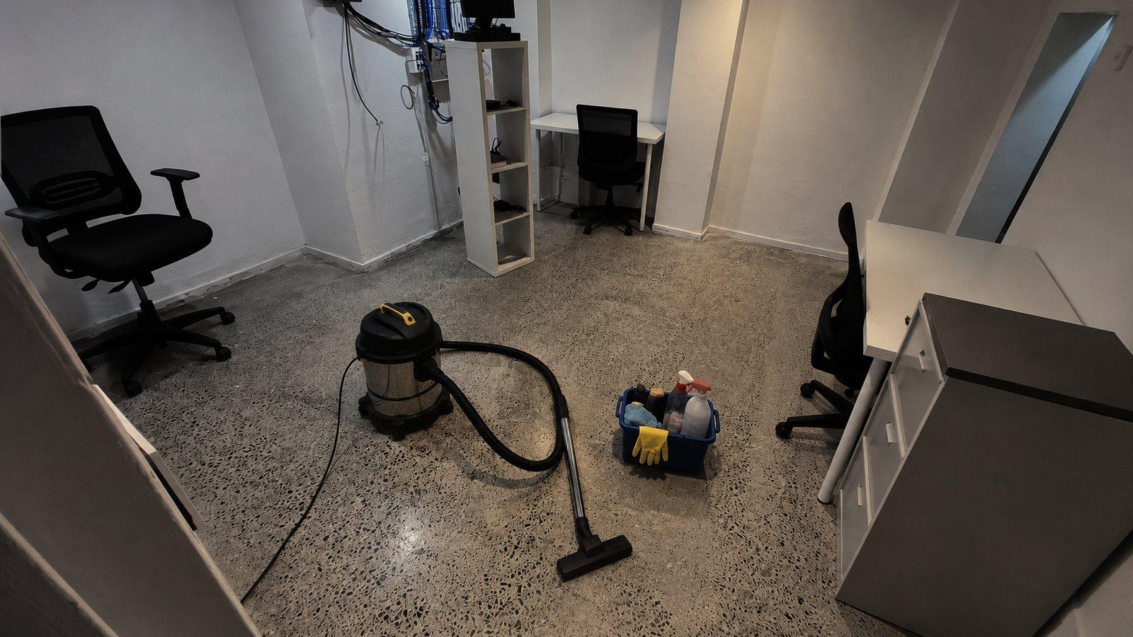 An office suite part way through a deep clean, desks and chairs pushed aside with a vacuum and a cleaning caddy out on the floor