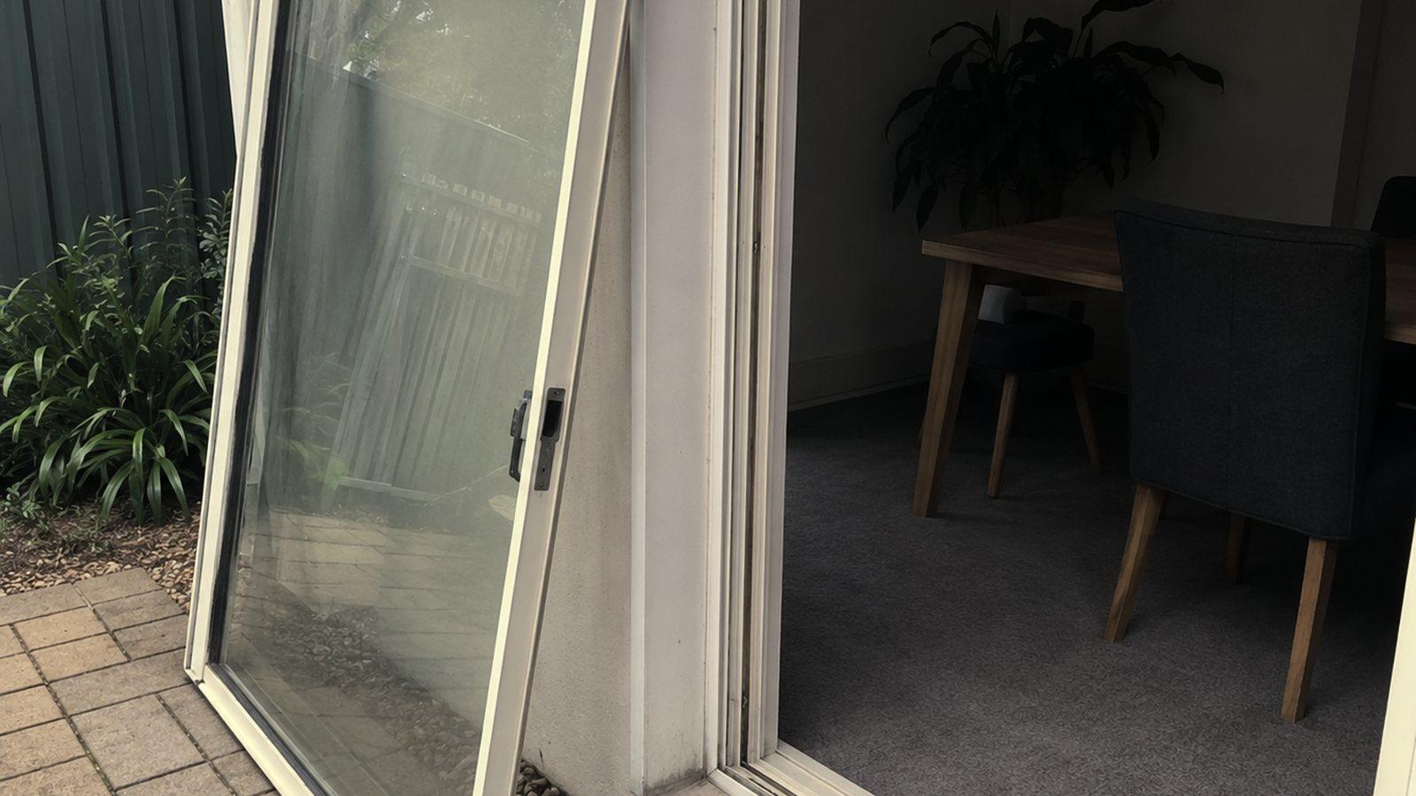 An aluminium sliding door panel lifted out of its opening and leaning on the paving beside the track