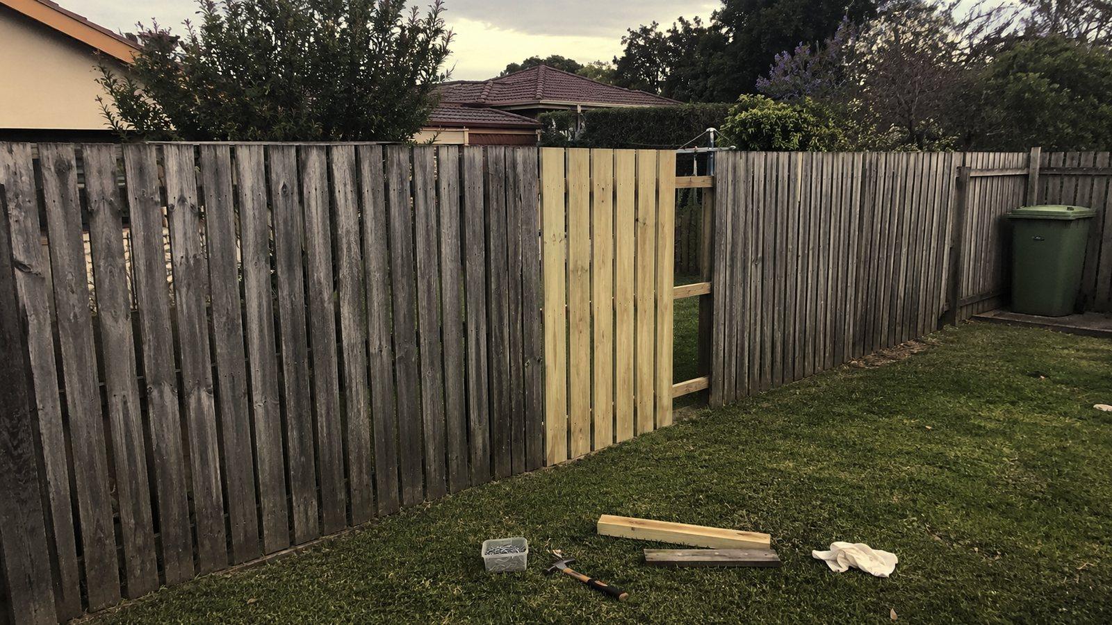 A timber paling fence run with a new section under repair