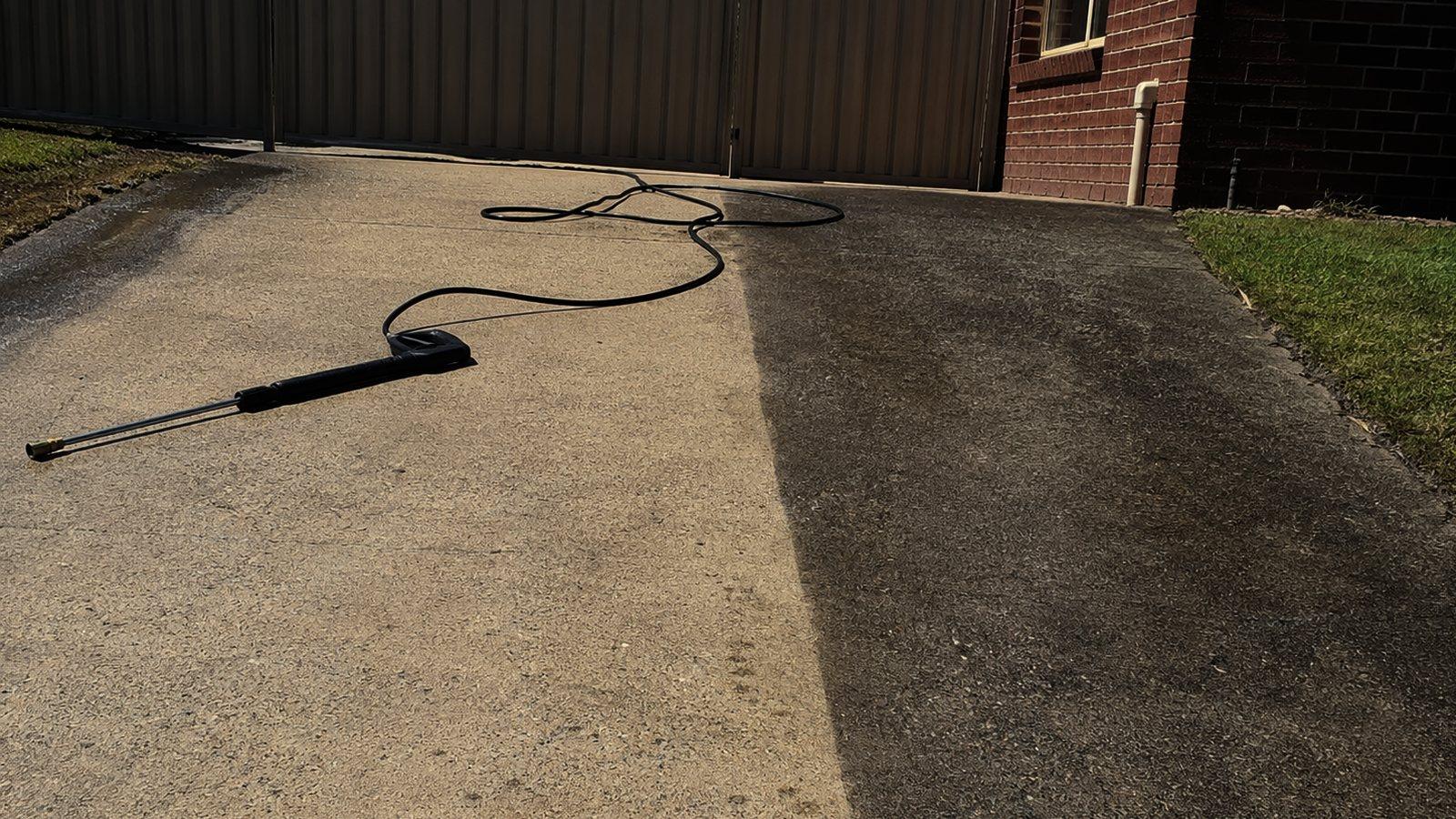 A pressure washer on grubby concrete pavers with a clean pale band already run behind it