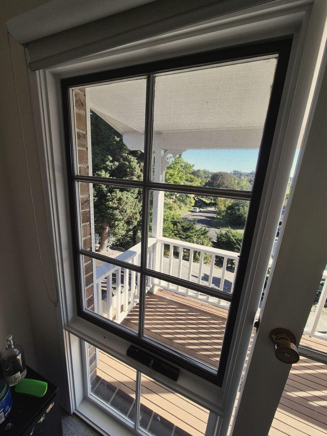 A glazed six pane timber door with intact flyscreen mesh and the deck beyond