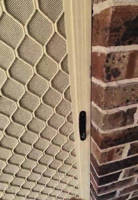 The latch side of a security screen door beside a brick reveal