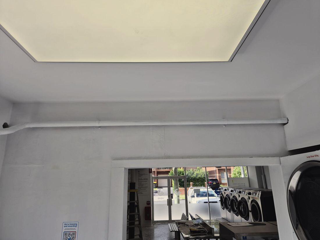 A laundromat ceiling, bulkhead and conduit painted out white, ladder still in shot