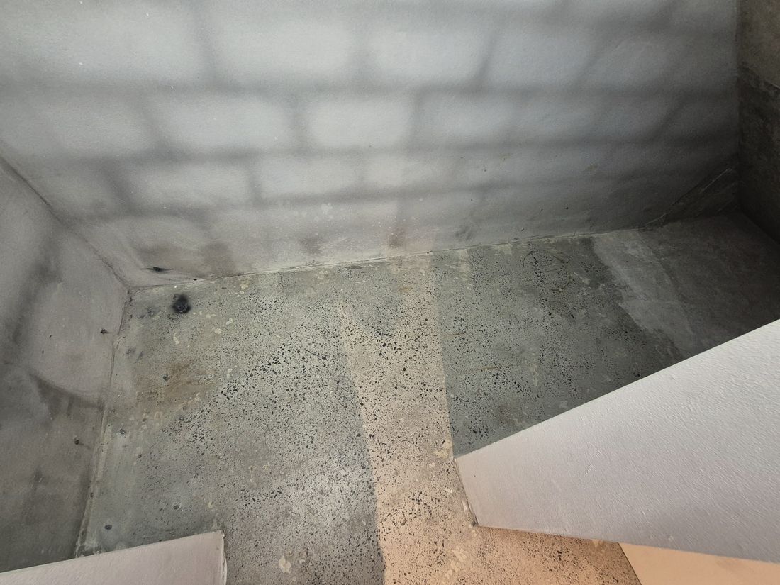 A grimy grey concrete floor with one pale cleaned strip cut through it, part way through a clean