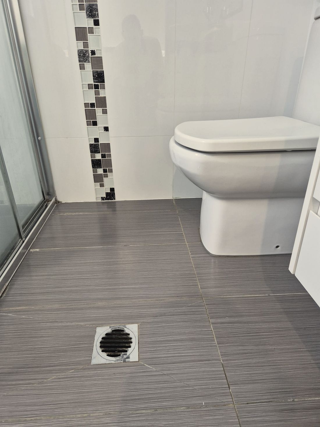 A tiled bathroom floor and wall with a mosaic feature strip